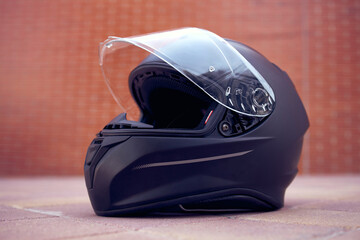 Close-up of a black helmet on the ground with the visor open. Side view.