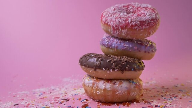 Pile of four tasty glazed sugar icing donuts with caramel topping falling down on pink background. Sweet buns. Delicious snacks. Sweetshop. Confectionery concept.