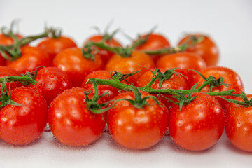 Cherry tomatoes on branch against white background.