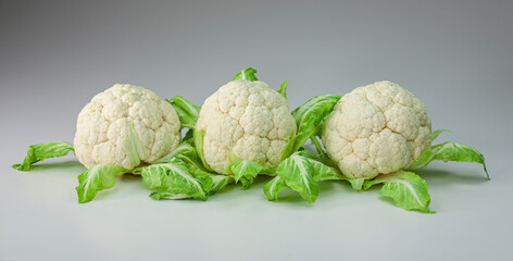 Three ripe cauliflowers with green leaves on white background