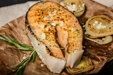 Grilled salmon steak with garlic, onion and herbs on a wooden cutting board. Close-up