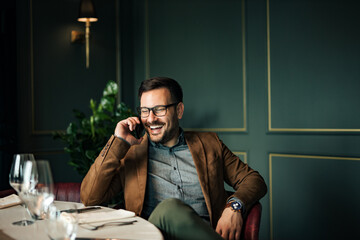 Portrait of a elegant man laughing while talking on smart phone in luxurious restaurant.
