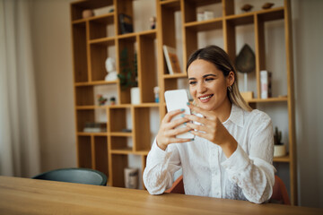 Smiling young businesswoman using smart phone in home office, portrait.