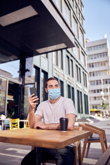 Man in mask is sittiing  with smartphone phone in cafe