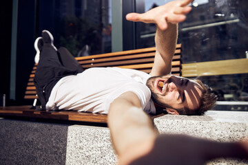  Laughing guy lying on a bench covering his face with his hand from sun close up