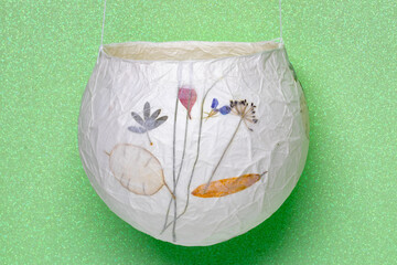 Lampion isolated. Close-up of a handmade paper lantern with floral pattern on a light green glitter...