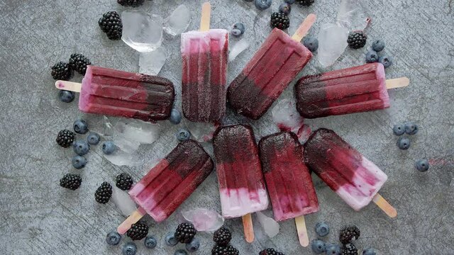 Homemade blackberry and cream ice-creams or popsicles with frozen berries on black slate tray