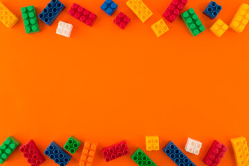 Pile toy colored plastic blocks and colored toy bricks on orange background. Copy space. Top view.