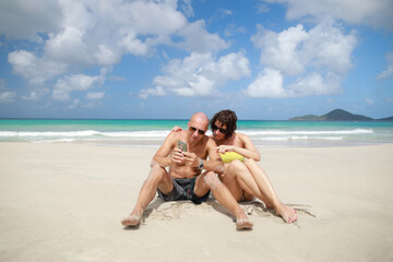 Man and woman siting on sand on beach in sunglasses and behind beautiful landscape of ocean in Mexico in Caribbean Sea