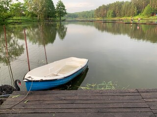 Obraz premium Wooden boat on the pier on the background of the lake. Fishing boat on the shore of a forest reservoir. The boat is tied to the shore. Concept: outdoor recreation, tranquility by the water.