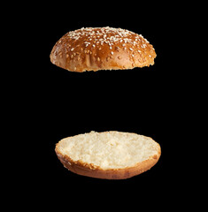 baked sesame seed round bun cut in half, halves fried and levitating in air over each other
