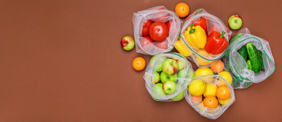 Fototapeta na wymiar Wide banner Fresh and juicy fruits and vegetables in reusable eco friendly mesh bags on the brown background. Plastic free, zero waste, and sustainable living concept. Reusable using. Copy space.