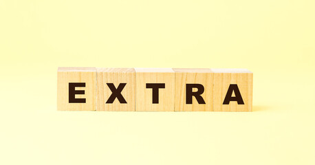 word extra with black letters on wooden blocks on yellow