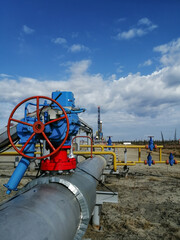 Pipeline fittings and manifold of producing gas wells in the field. Handwheels for high pressure valves. In the background, a drilling rig. Blurring distant objects.