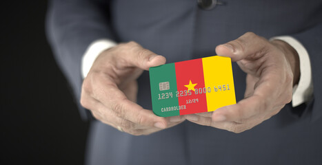 Businessman holding plastic bank card with printed flag of Cameroon, fictional numbers