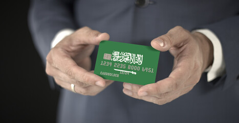 Businessman holding plastic bank card with printed flag of Saudi Arabia, fictional numbers