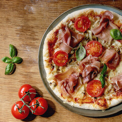 Fresh baking homemade pizza napolitana with prosciutto ham, cheese, tomatoes, basil on plate over...