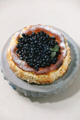 Homemade blueberry baked soft cheesecake san sebastian on ceramic cake stand plate decorated by fresh wild berries, icing sugar and mint over white texture background. Copy space