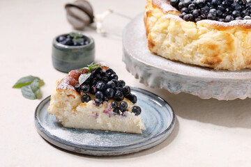 Homemade blueberry baked soft cheesecake san sebastian, whole and sliced, on ceramic cake stand plate decorated by fresh wild berries, icing sugar and mint over white texture background.