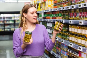 Smiling girl choosing spanish green olives during grocery shopping at food department in supermarket