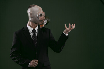 Portrait of a man wearing a business suit and an old gas mask holding his left hand up, isolated on dark green background.