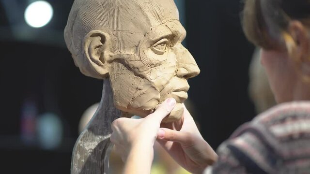 Woman sculptor at work on a sculpture of a human head. The process of restoring the shape of jawbone. Side view. Close up view.