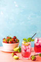 Strawberry mojito cocktail with ice in two glasses with water drops on light blue color background, pink board. Copy space, summer vacation and party concept