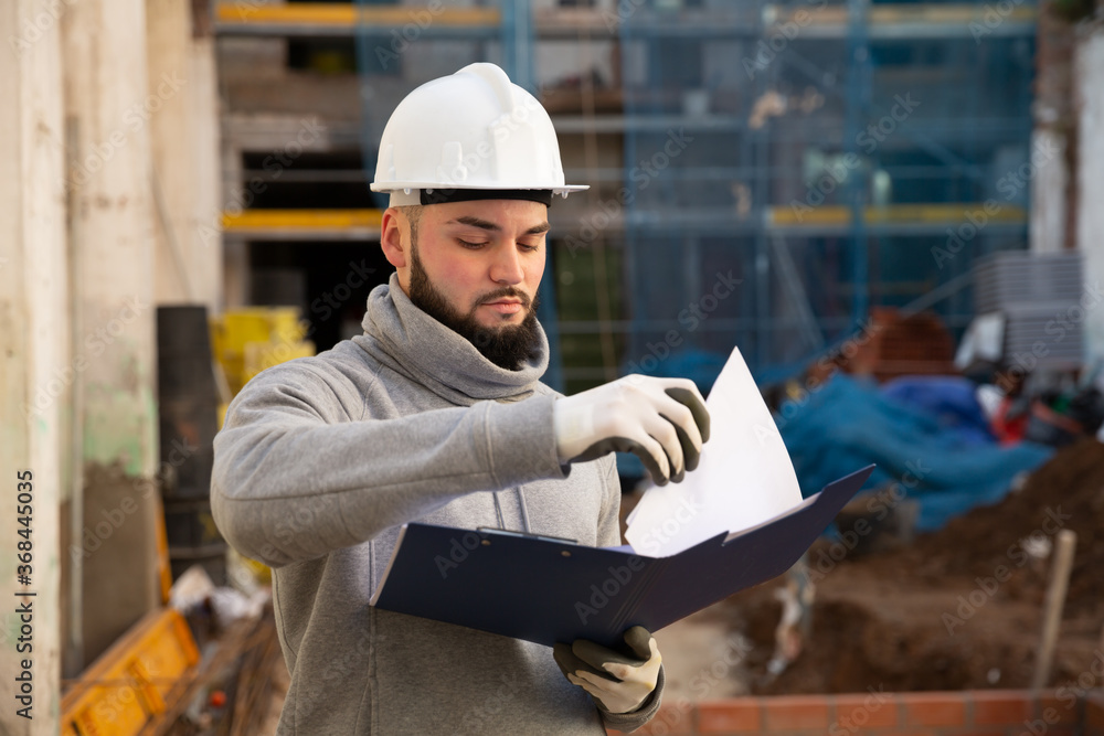 Wall mural Young bearded foreman making task list during works in building under construction