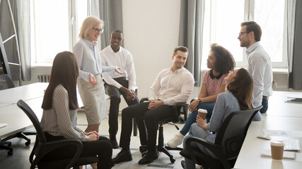 Mature businesswoman holding business briefing with diverse employees, coach training staff, team...
