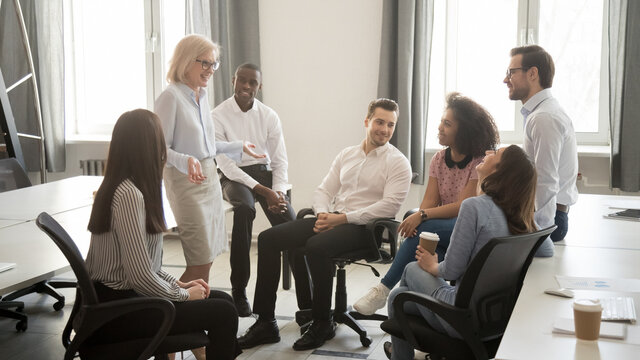 Mature businesswoman holding business briefing with diverse employees, coach training staff, team leader with colleagues discussing strategy, involved in team building activity, horizontal banner