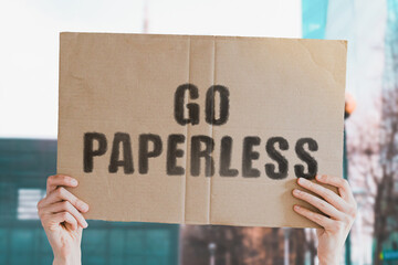 The phrase " Go paperless " on a banner in men's hand with blurred background. Human impact on the environment. Environmental degradation. Nature. Forest. Trees. Modern technology