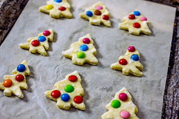 Christmas tree cookies with multicolored dough candies before baking on a sheet of parchment,