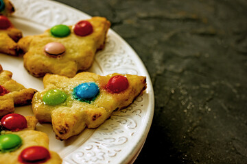 Colorful christmas homemade christmas tree cookies on white plate on dark background, copy space