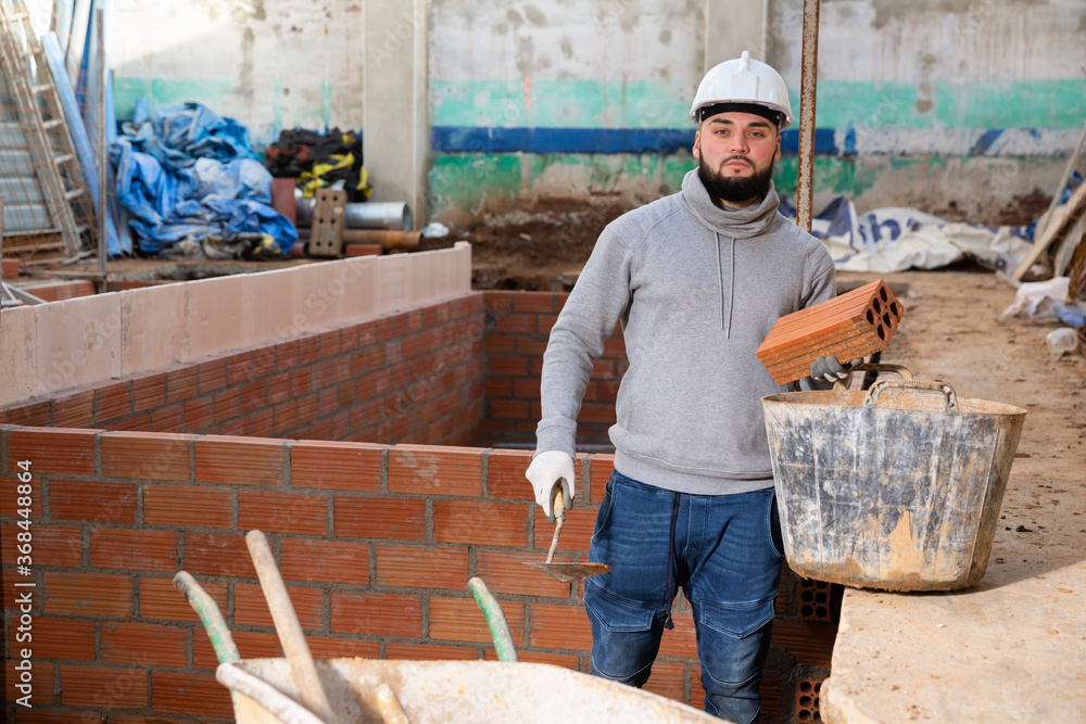 Wall mural Focused young man working on his house renovations, installing brick wall inside ..