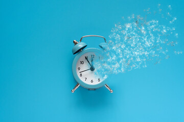 Alarm clock with dispersion effect on blue background. Quarantine or passing away concept. Top view. Flat lay