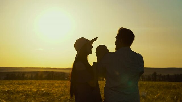 Silhouettes of mother and father holding baby in wheat field at sunset