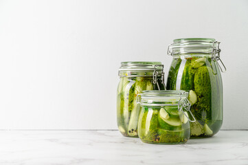 Healthy probiotic vegan food. Three glass jars of homemade fermented cucumbers with garlic, dill and pepper. Light gray background. Copy space.