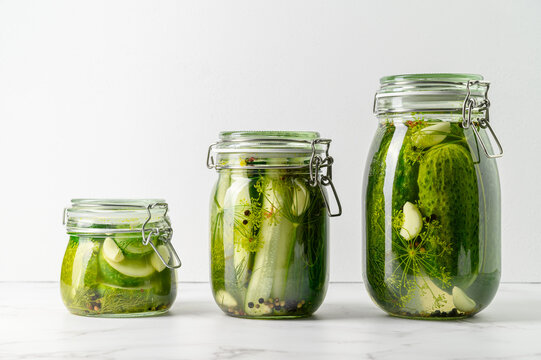 Healthy probiotic vegan food. Three glass jars of homemade fermented cucumbers with garlic, dill and pepper. Light gray background. Copy space.