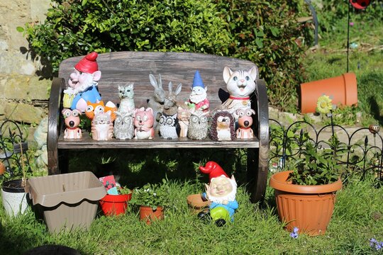 Some Kitsch Garden Ornaments And Gnomes Lined Up On A Bench.