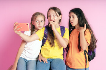 Three teen girls smiling and shoots a video on a pink background.  Selfies