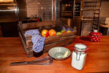 Kitchen utensils, wooden box of ripe apples, saucepan, sugar in jar and butter
