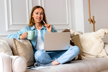 Happy woman on sofa with laptop working at home