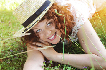 portrait d'une jeune et jolie femme rousse souriante allongée dans l'herbe en été 