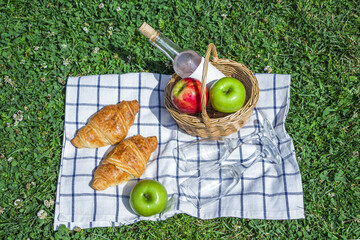 Romantic summer picnic lunch outdoors. Wicker basket with croissants, apples and bottle of rose...