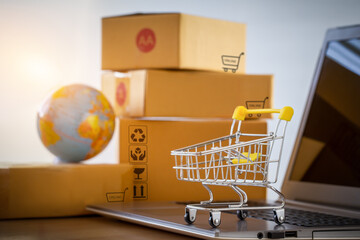 Shopping cart or trolley  on a notebook computer placed in front of the parcel box for delivery to...