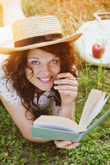 jeune et jolie femme rousse allongée dans l'herbe et lisant un livre 