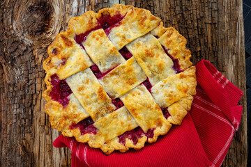 A fresh baked strawberry rhubarb pie with overlay crust on a barn plank wood table ready to slice and eat for a favorite dessert in Michigan, USA.