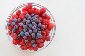 On the white tabletop is a glass plate with red raspberries and blue Irga berries
