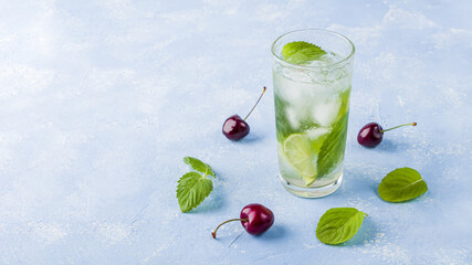 Refreshing cool detox drink with lime and mint on blue background. Glass of Summer lemonade or ice tea decorated with cherries. Mojito cocktail with ice cubes. Healthy eating. Сopy space for text