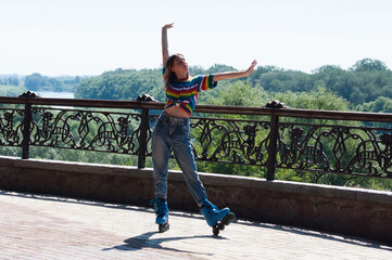 Cheerful teenage girl on roller skates posing in the park on a warm summer morning